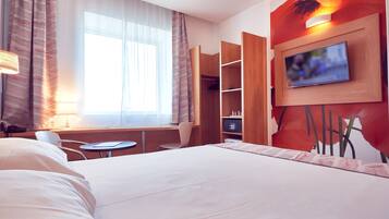 A hotel room with a large bed, a desk with a chair, a TV mounted on the wall, and a wardrobe.