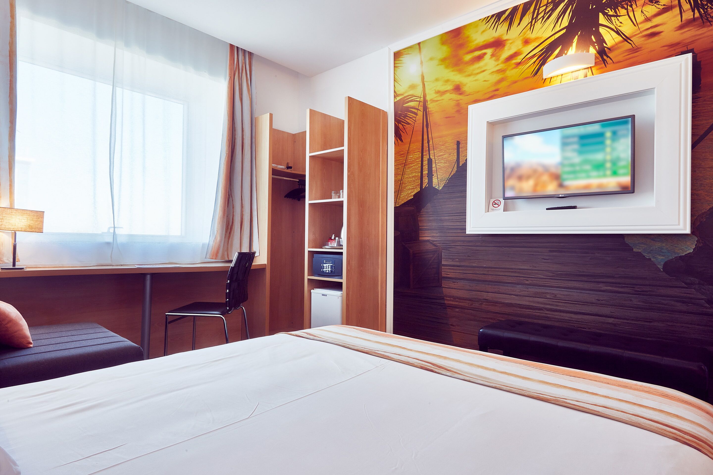 A hotel room with a bed, a desk, a chair, a TV, and a wardrobe.