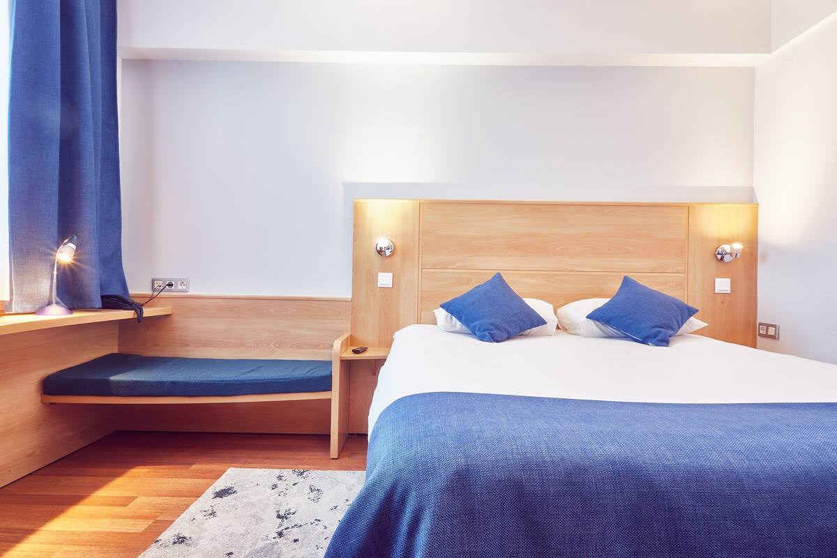 A modern bedroom with a wooden headboard, a single bed with blue bedding, a bedside table, and a nightstand with a lamp.