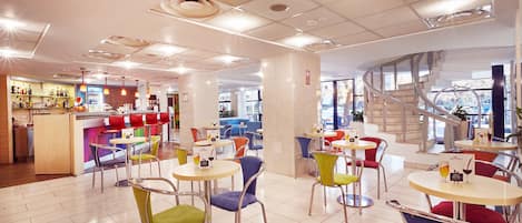 Una cafetería moderna con mesas redondas y sillas coloridas, una zona de bar y una escalera en espiral.