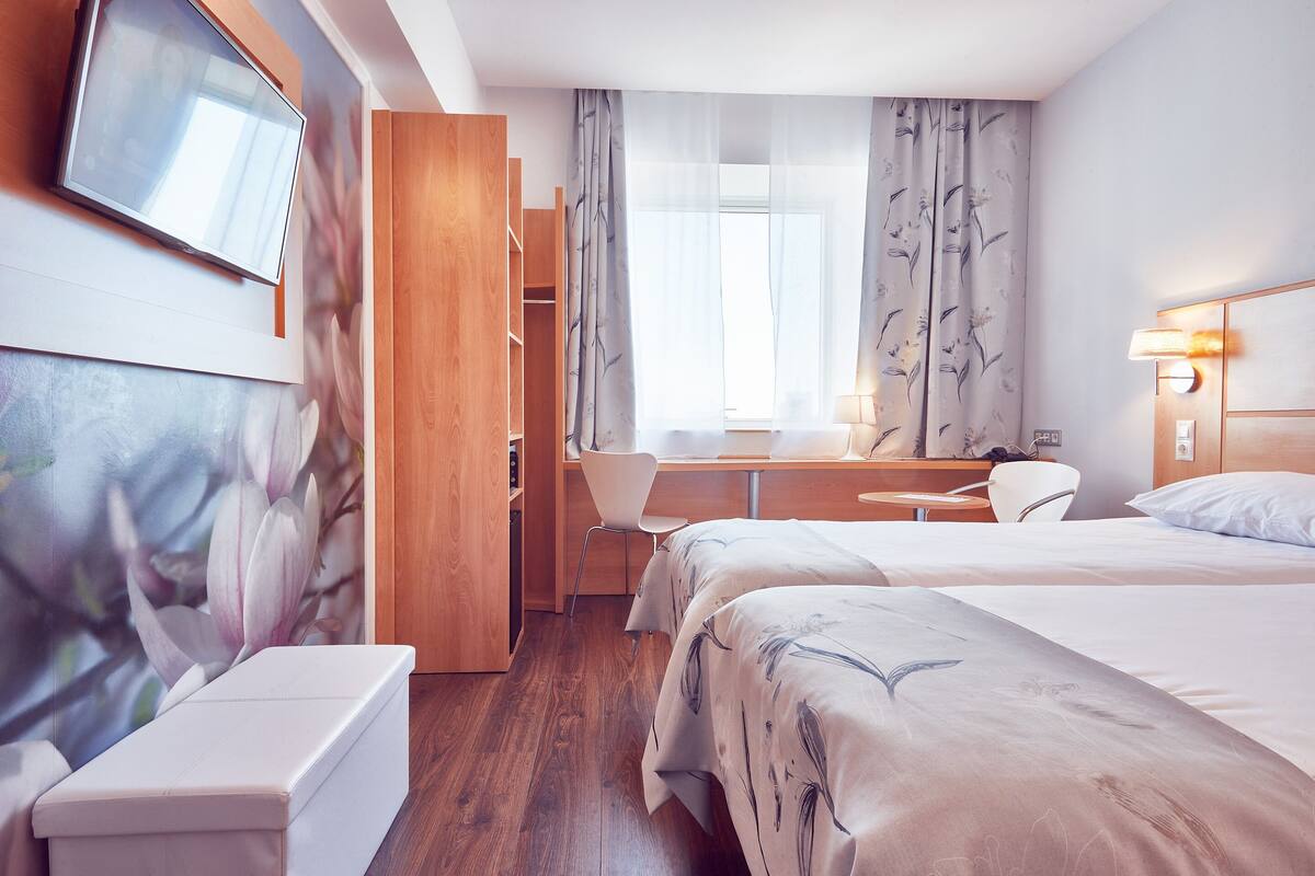 A hotel room with a bed, a desk, a chair, a TV, and a wardrobe.