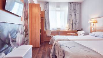 A hotel room with a bed, a desk, a chair, a TV, and a wardrobe.