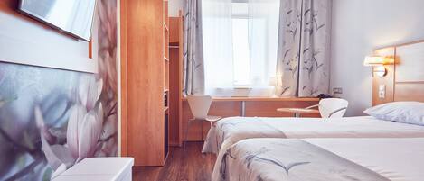 A hotel room with a bed, a desk, a chair, a TV, and a wardrobe.