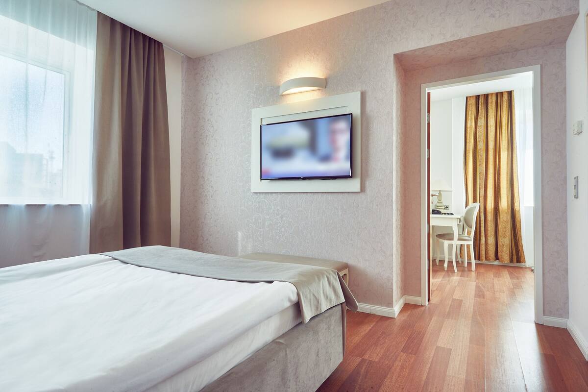 A hotel room with a bed, a television mounted on the wall, and a desk with a chair in the adjacent room.