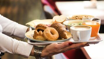 A tray with croissants, a muffin, a bowl of cereal, a cup of coffee, and a glass of orange juice.
