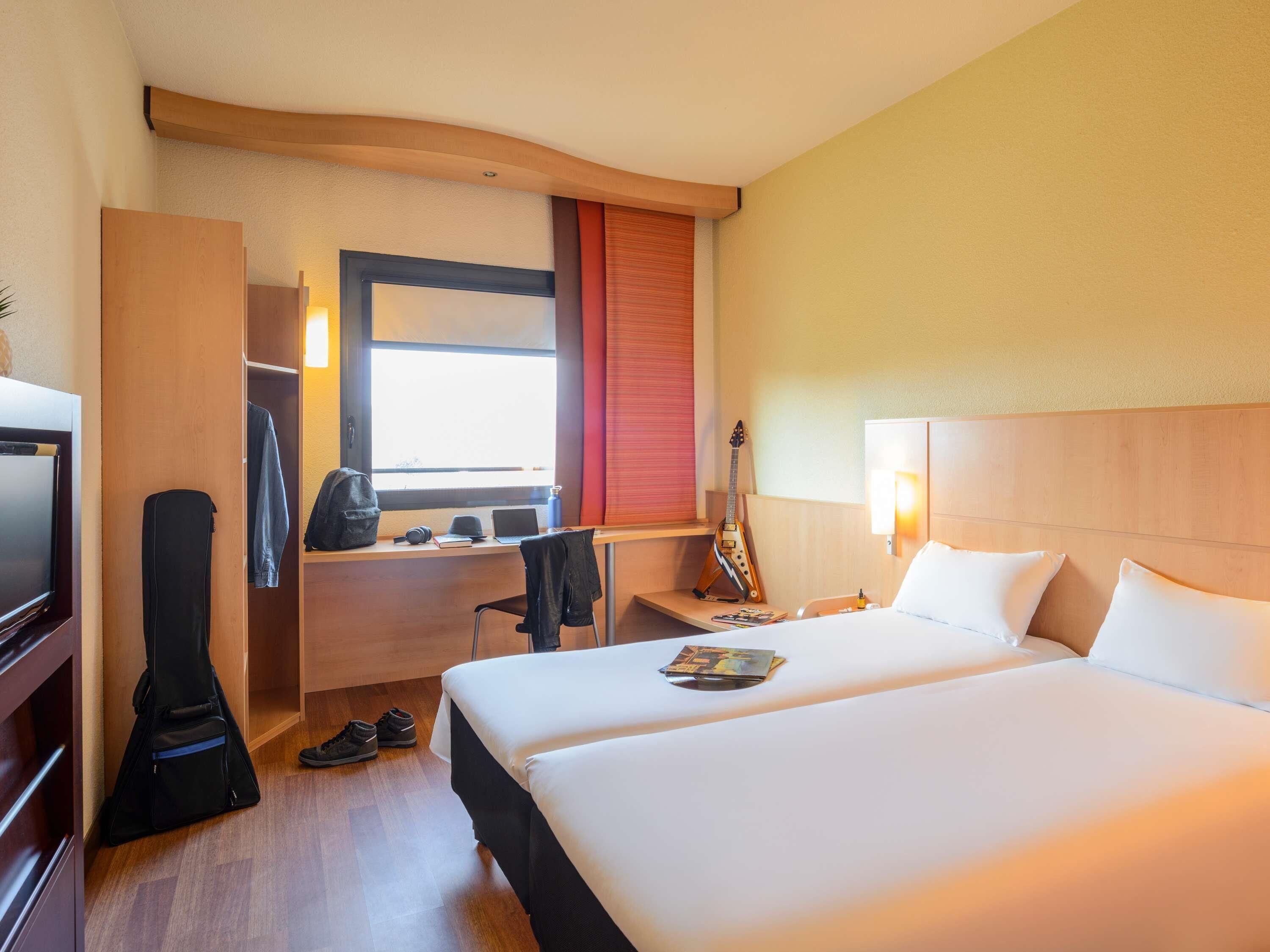Une chambre d’hôtel avec un lit, un bureau avec un ordinateur portable, une guitare et un téléviseur.