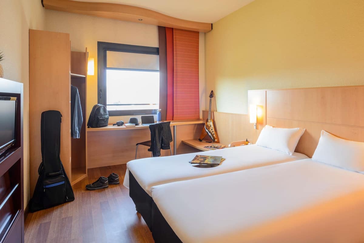 Hotellihuone, jossa on sänky, työpöytä kannettavalla tietokoneella, kitara ja televisio.