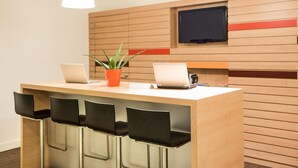 Een moderne receptiezone met een houten receptiebalie, twee laptops, een potplant en een flatscreen televisie aan de muur.