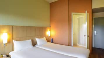 Una camera d'albergo con un letto grande, due abat-jour, un comodino con un telefono e una bottiglia, e una porta che dà su un'altra stanza.