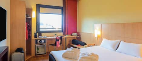 A hotel room with a bed, a desk, a chair, a television, a minibar, and a window with a view.