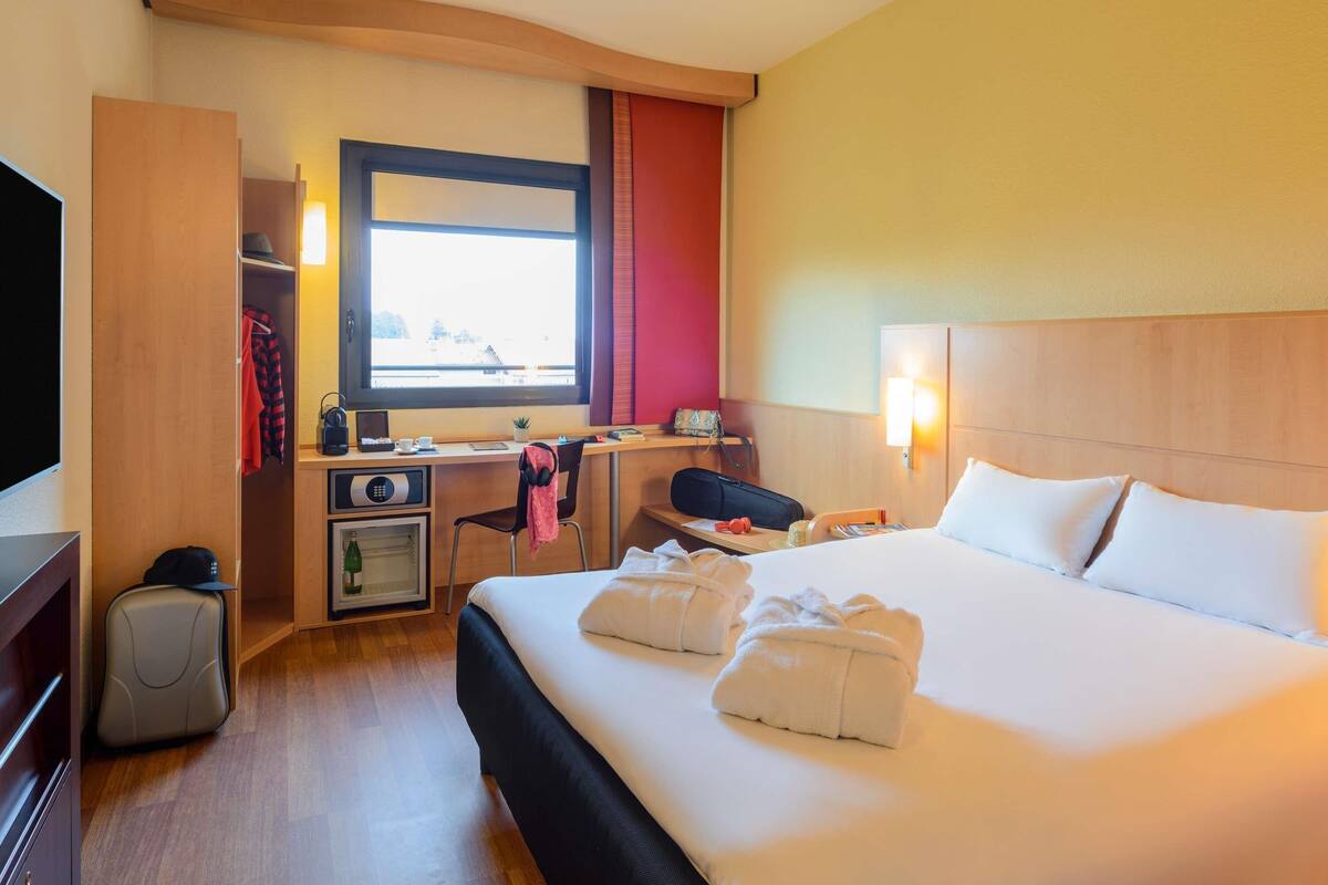 Een hotelkamer met een bed, een bureau, een stoel, een televisie, een kledingkast en een raam met uitzicht.