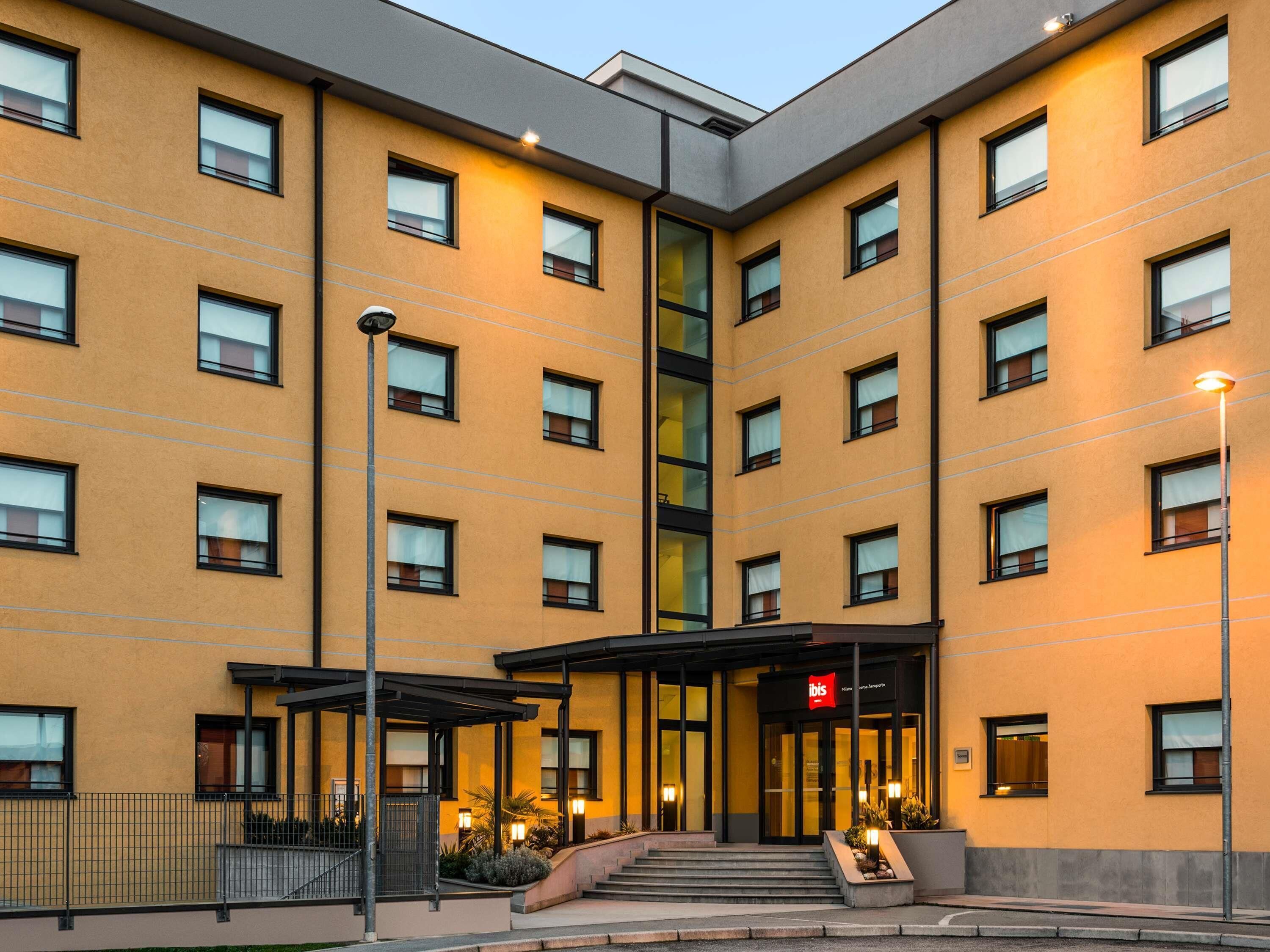 A multi-story hotel with a yellow facade, large windows, and a central entrance with steps leading up to it.