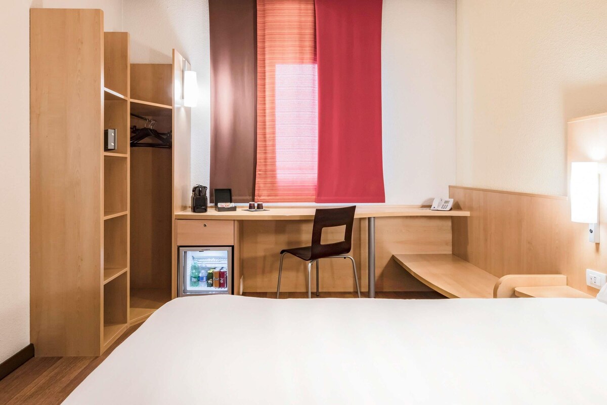 Ein Hotelzimmer mit Bett, Schreibtisch, Stuhl, Kleiderschrank und einem kleinen Kühlschrank.