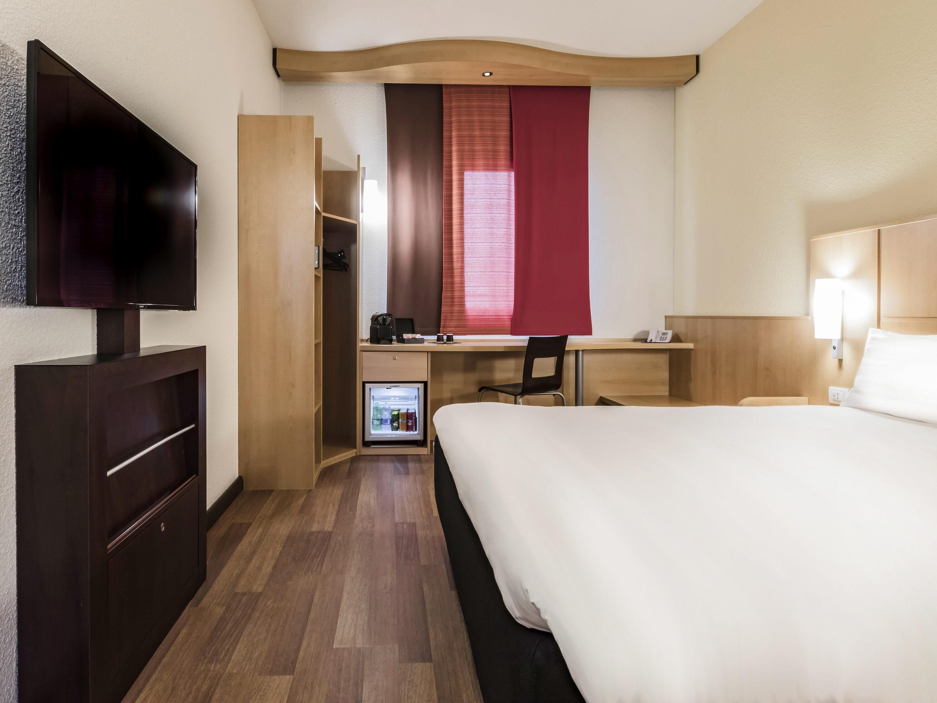 Une chambre d’hôtel comprenant un lit, un bureau avec une chaise, une télévision, une armoire et un mini-réfrigérateur.