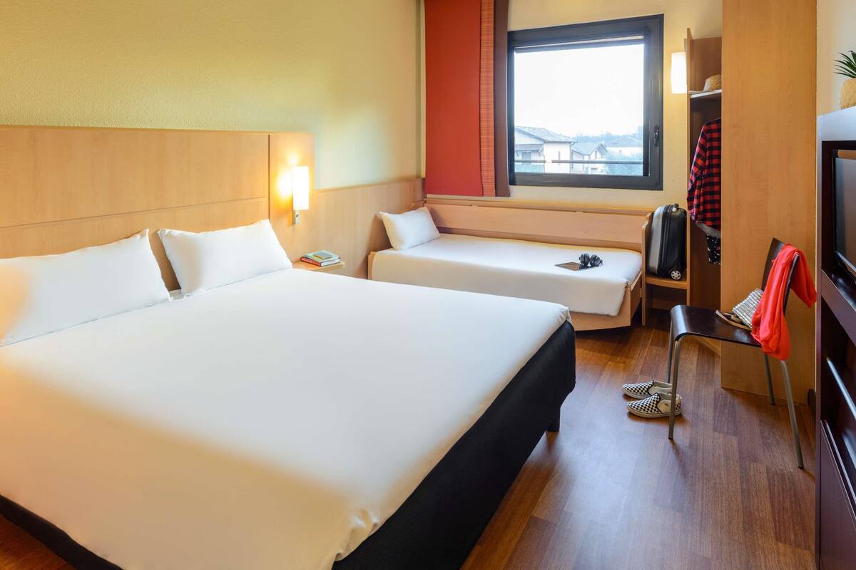 Een hotelkamer met twee bedden, een televisie, een raam met uitzicht en een bureau met stoel.