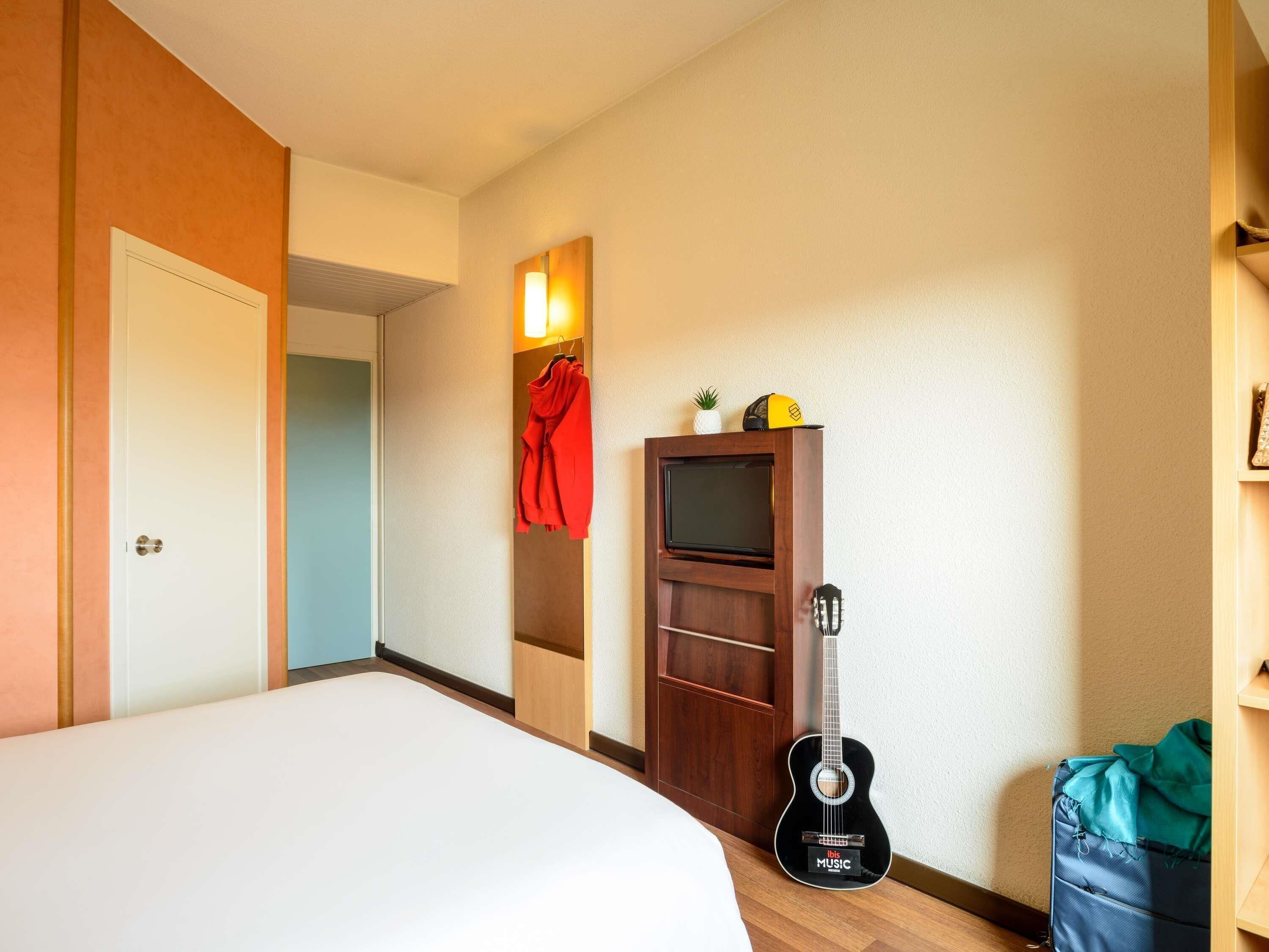 Une chambre d’hôtel avec un lit, une guitare, une télévision et une armoire.