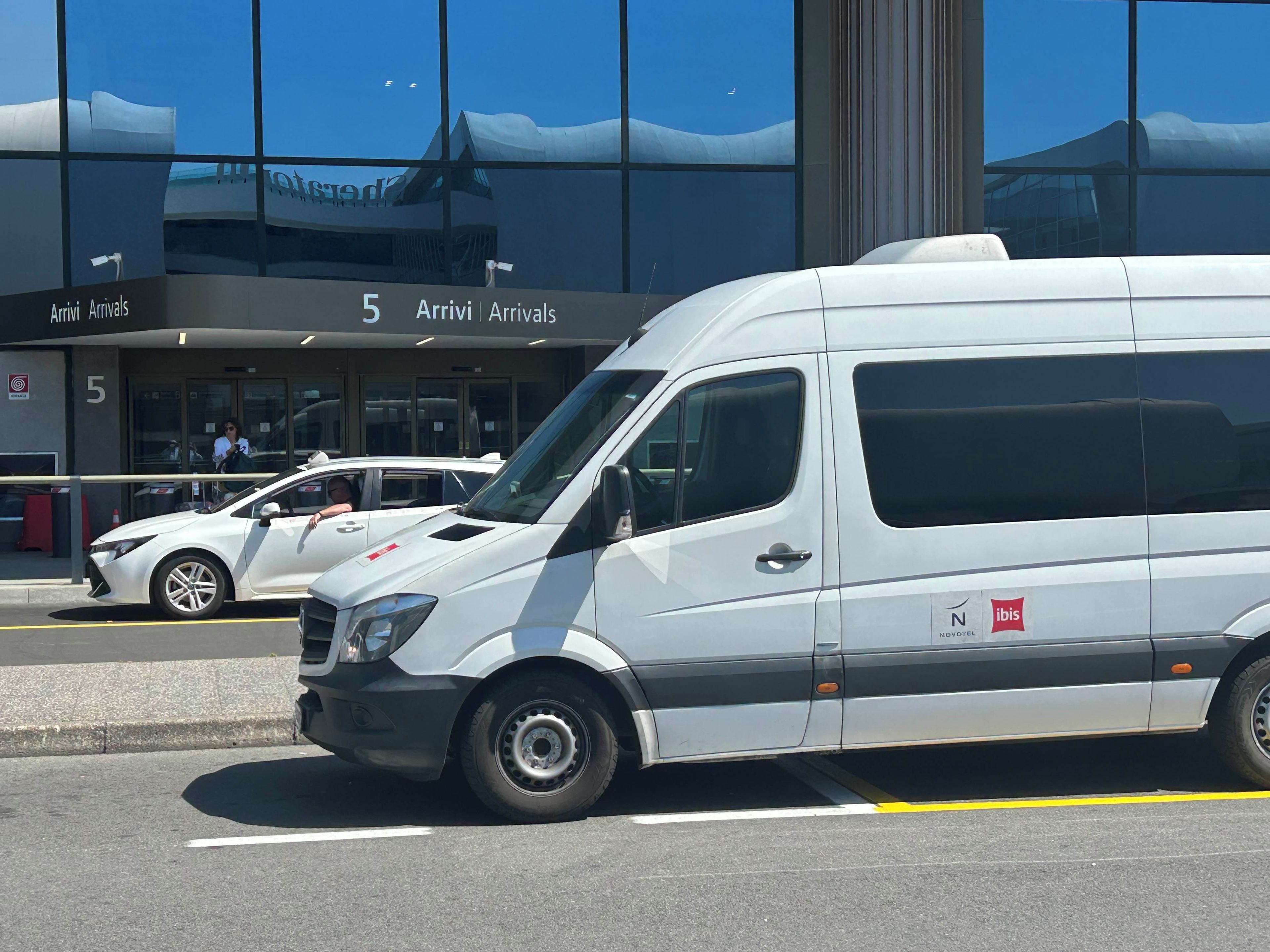 Un furgone bianco parcheggiato di fronte a un edificio con un cartello che indica 'Arrivi'.