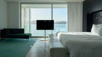 Habitación de hotel moderna con una cama grande, un sofá, un televisor y vista al mar.