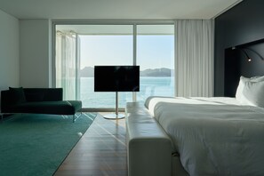 Habitación de hotel moderna con una cama grande, un sofá, un televisor y vista al mar.