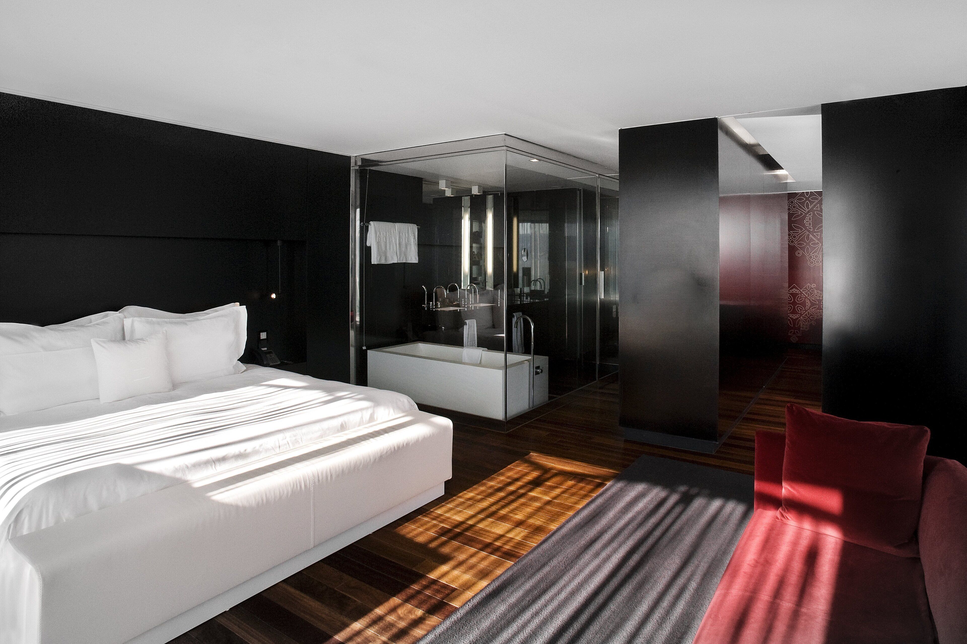 Een moderne hotelkamer met een groot bed, een douchecel met glazen wanden en een rode accentmuur.
