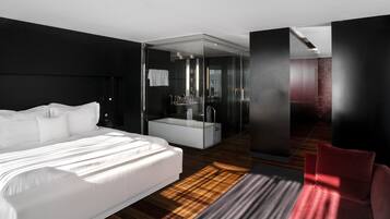 Een moderne hotelkamer met een groot bed, een douchecel met glazen wanden en een rode accentmuur.