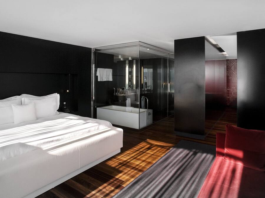 Een moderne hotelkamer met een groot bed, een douchecel met glazen wanden en een rode accentmuur.