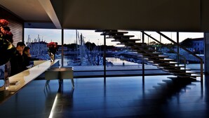 Un interior moderno con vista a un puerto deportivo, una escalera y una recepción.