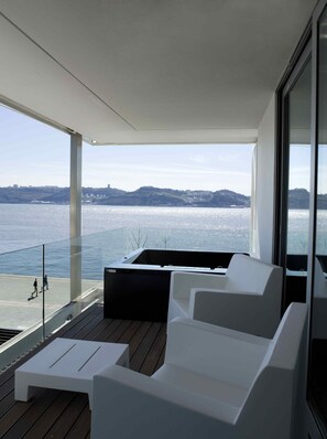 Un balcón moderno con mobiliario blanco, vista al mar y cielo despejado.