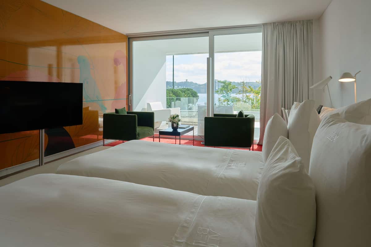 Habitación de hotel con dos camas, televisión, balcón con vistas al paisaje y diseño de interiores moderno.
