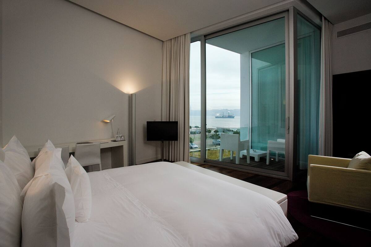 Habitación de hotel con una cama grande, un escritorio con silla, televisor y balcón con vista a la ciudad.