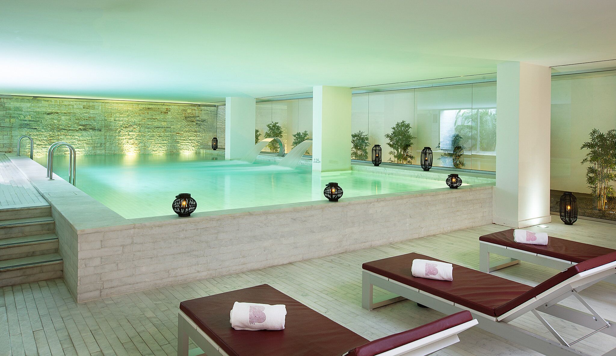 A spa area with a pool, lounge chairs, and a stone wall.
