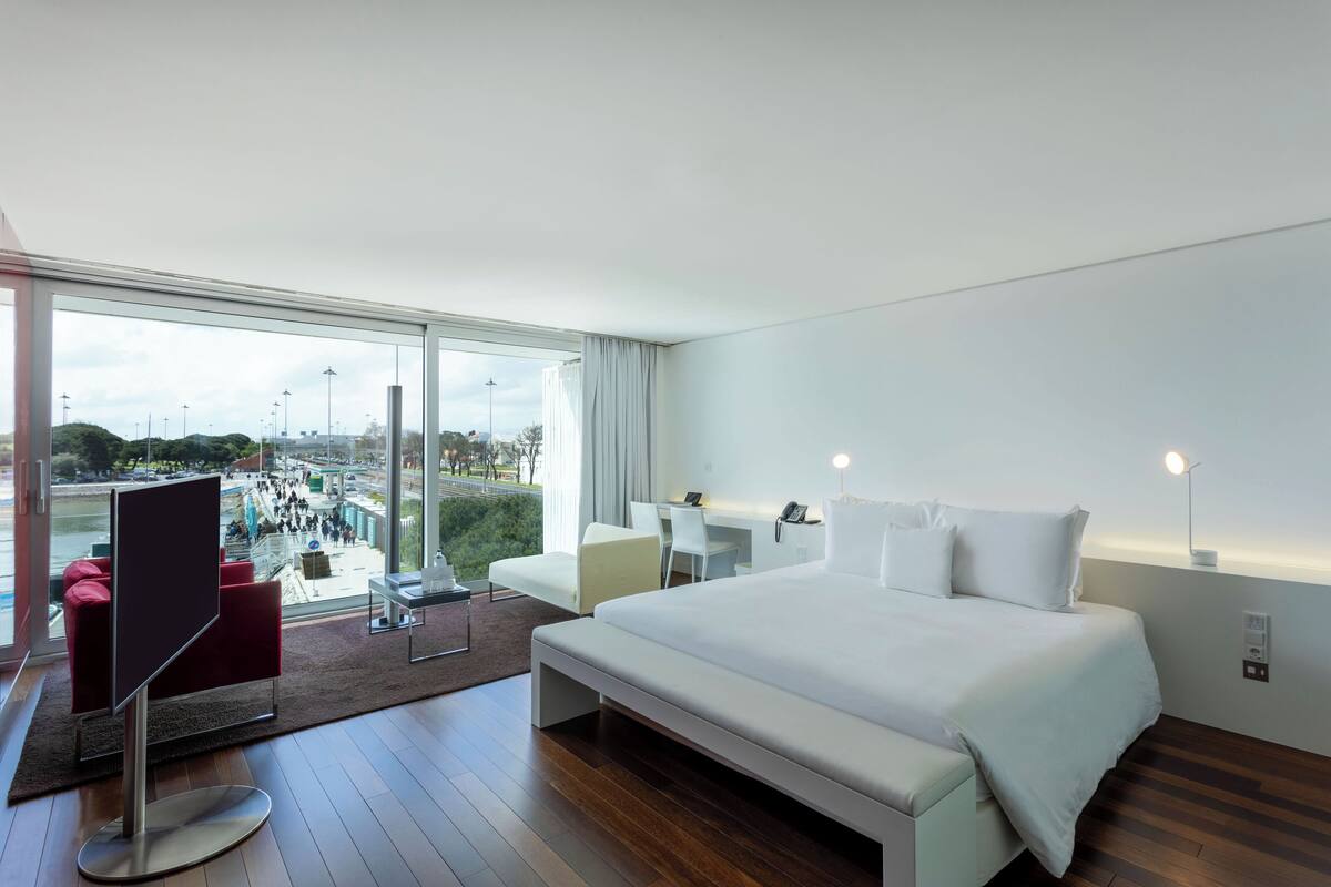 Una habitación de hotel moderna con una cama grande, un escritorio y vistas a un paisaje urbano.