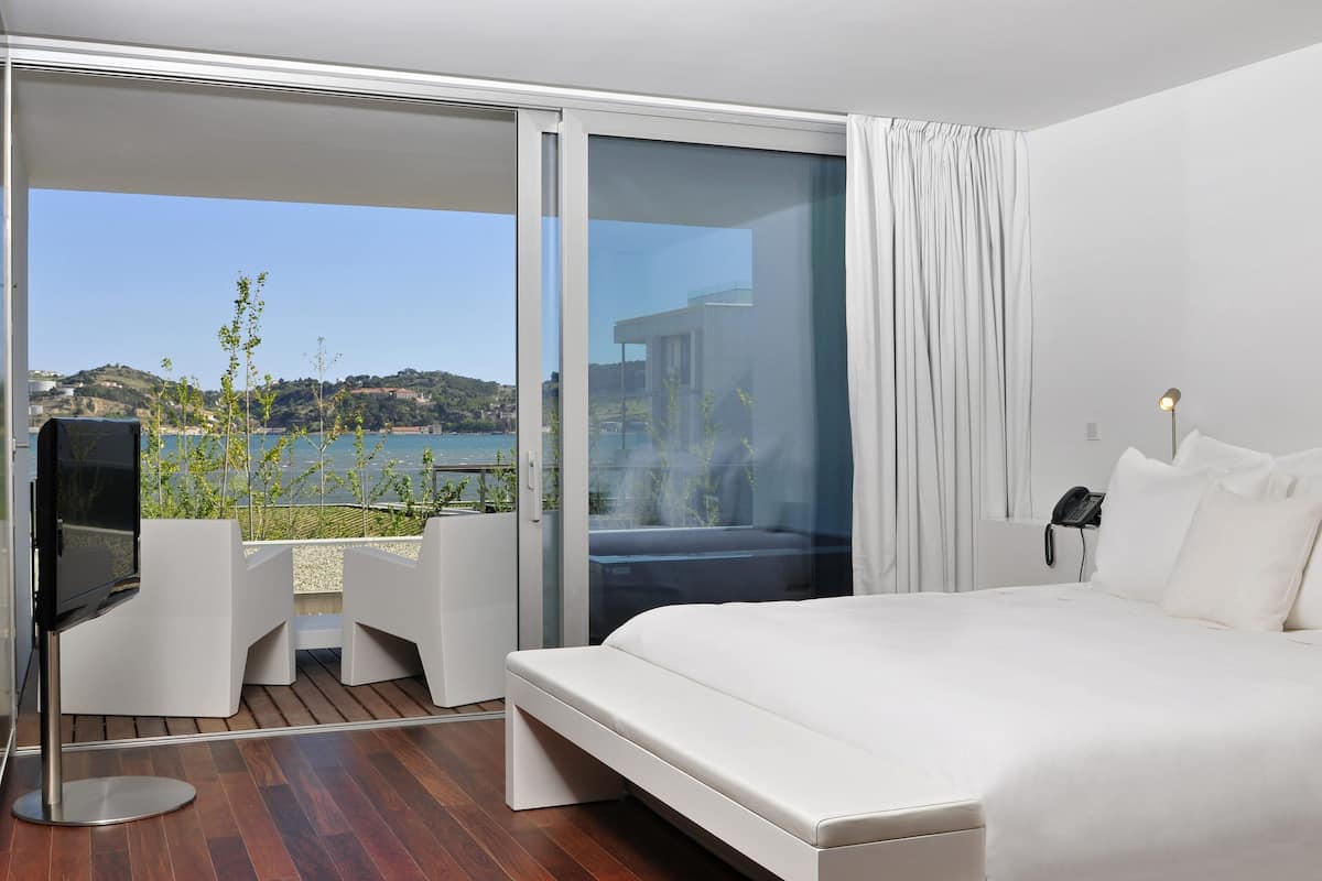 Una habitación de hotel moderna con una cama grande, un televisor, un balcón con vistas al mar y un teléfono en la pared.