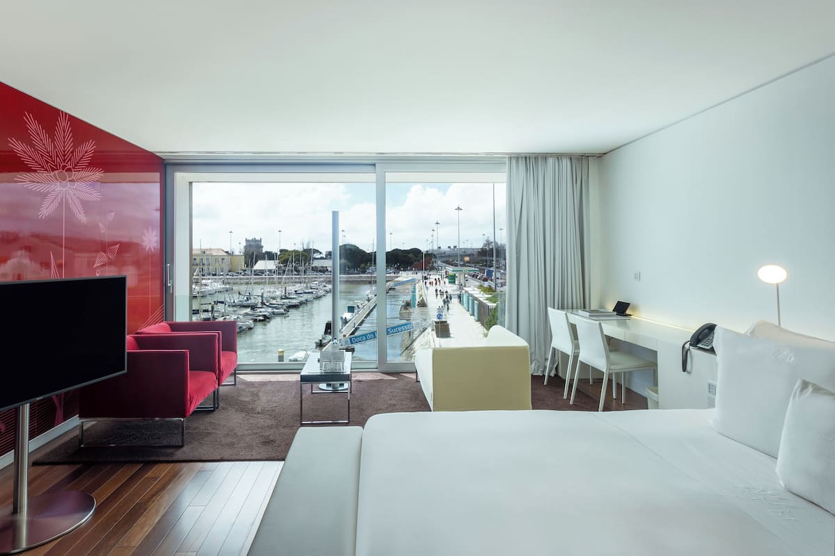 Una habitación de hotel moderna con una televisión grande, una cama, un escritorio con una silla y vistas a un puerto deportivo.