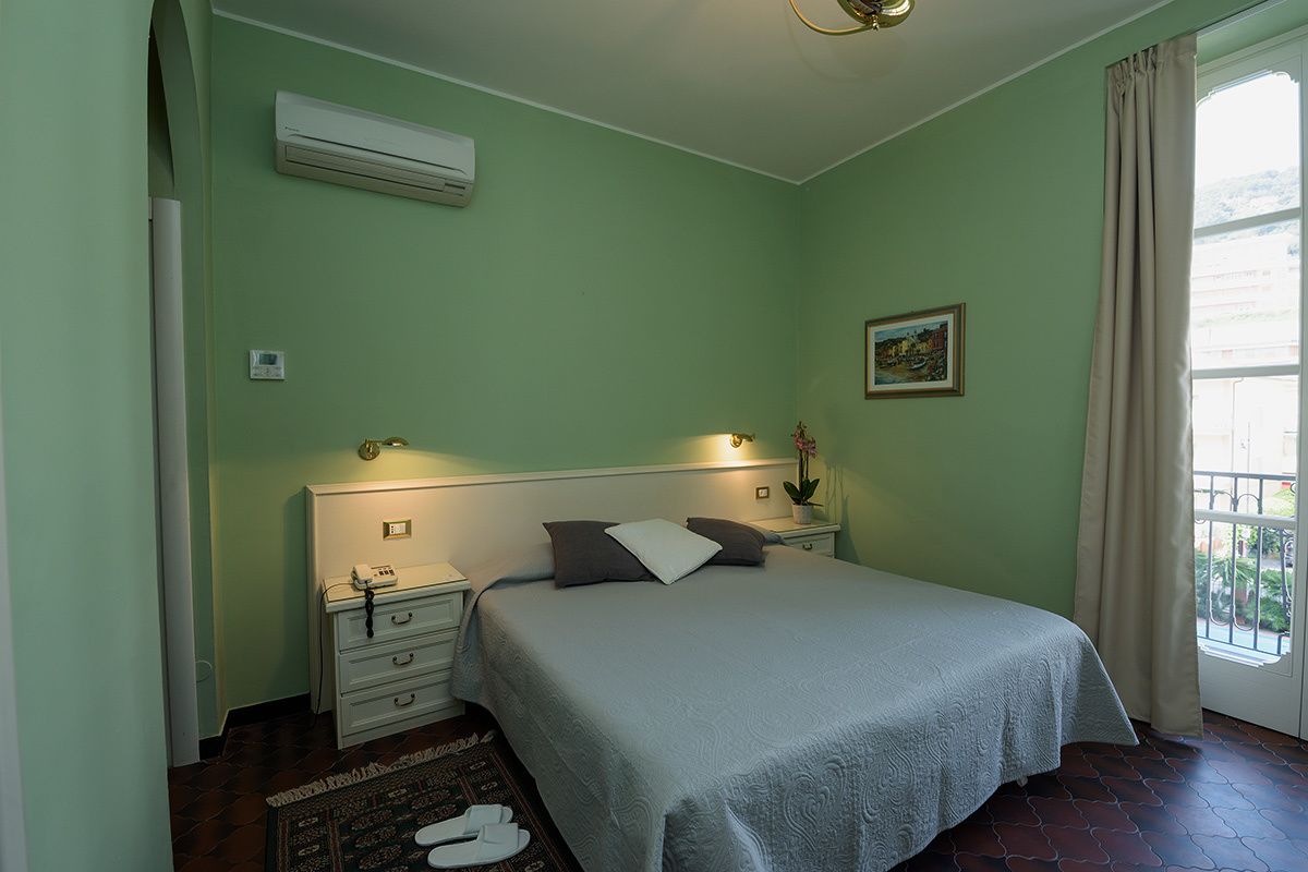 Ein Schlafzimmer mit Bett, Nachttischen, einer Klimaanlage, einem Fenster mit Vorhängen und einem kleinen Bild an der Wand.