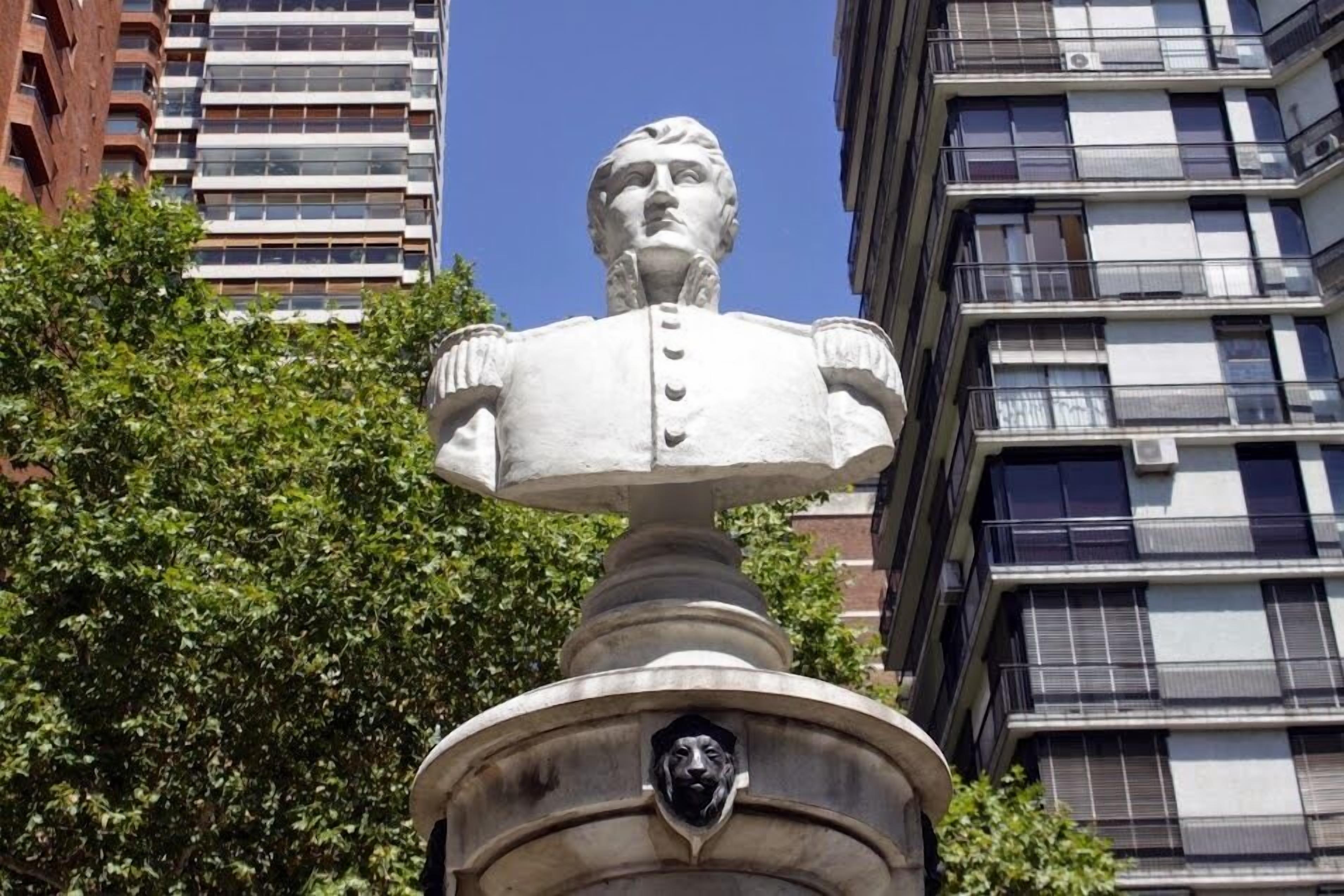 Busto sobre pedestal, con un edificio al fondo.