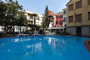 A swimming pool with lounge chairs, surrounded by multi-story buildings with balconies and a clear sky. - Hotel SplendidMare (Laigueglia)