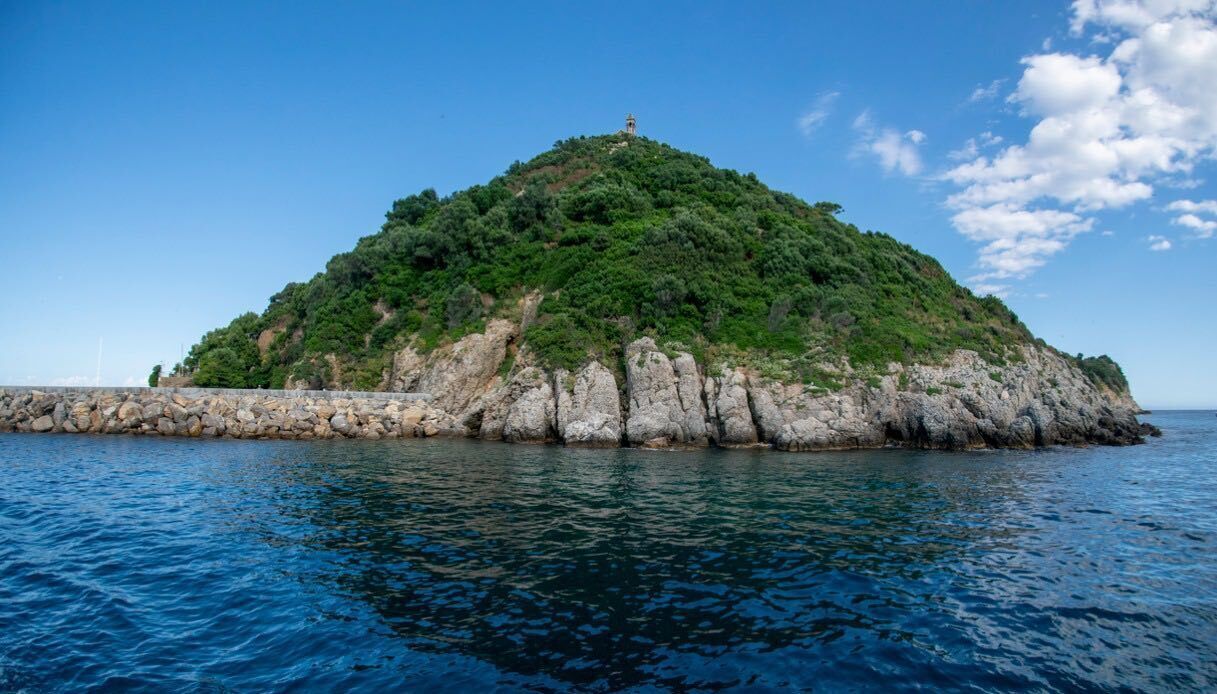 Eine felsige Insel mit einem Leuchtturm auf der Spitze, umgeben von klarem, blauem Wasser.