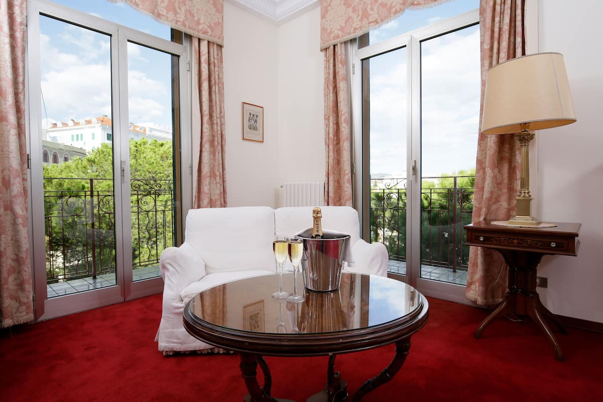 Een kamer met een witte bank, een ronde tafel met een champagnefles en glazen, en een lamp.