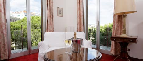 A room with a white sofa, a round table with a champagne bottle and glasses, and a lamp.