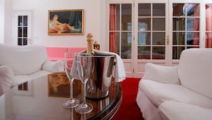 Una habitación con un sofá blanco, una mesa de vidrio con una botella de champán y copas, y un cuadro en la pared.