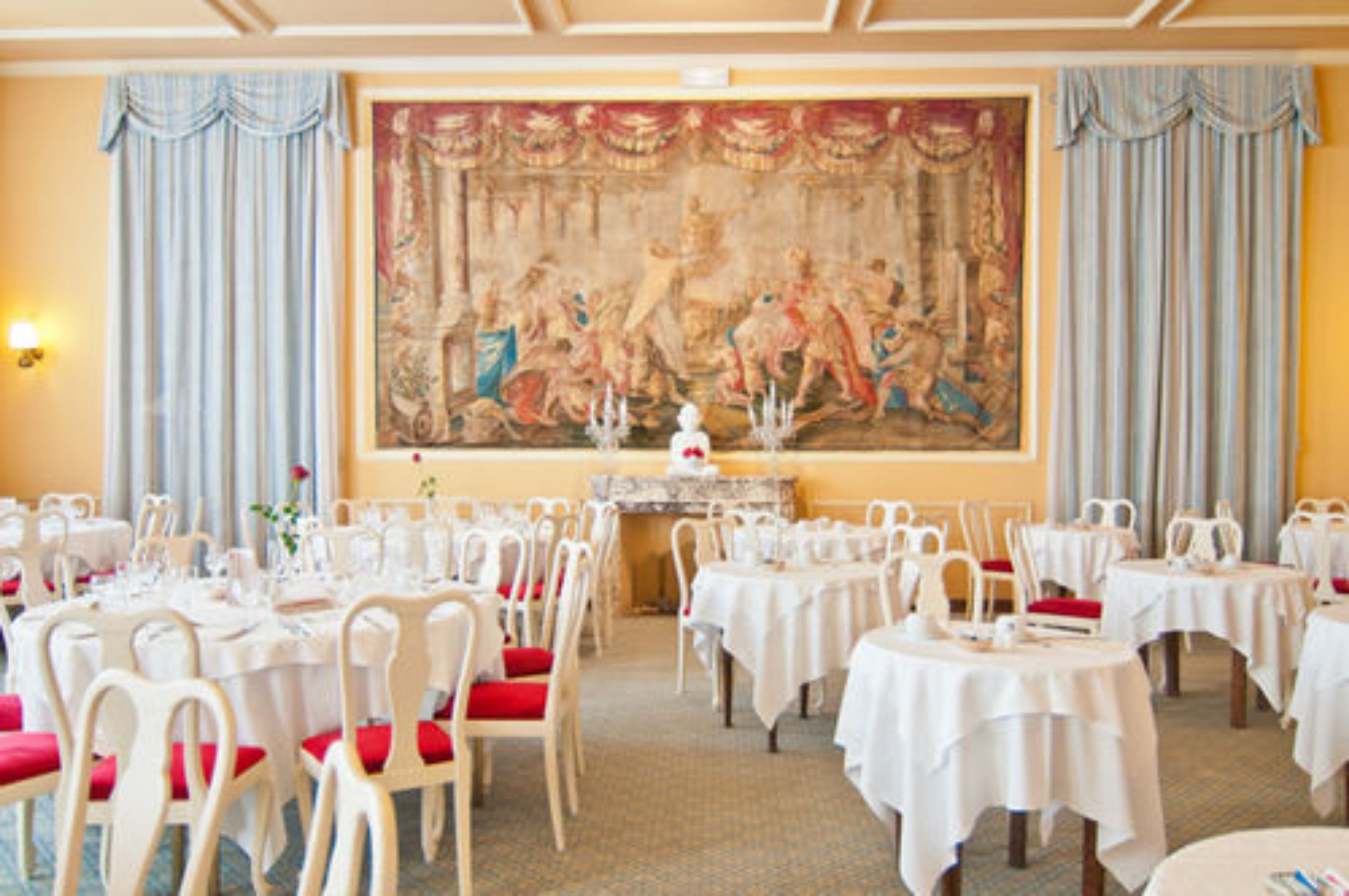 Ein Essbereich mit runden Tischen, weißen Stühlen und einem großen Gemälde im klassischen Stil an der Wand.