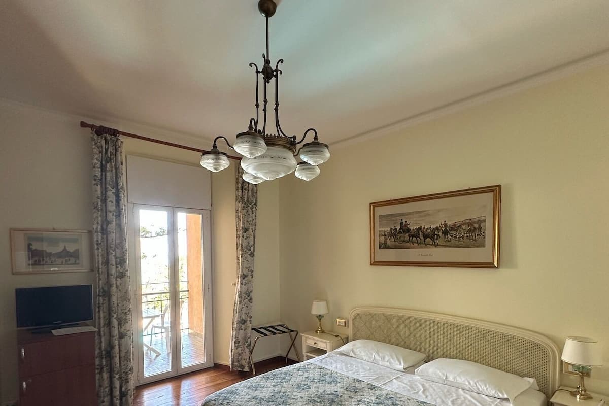 Een slaapkamer met een bed, een kroonluchter, een televisie, een bureau en een ingelijst schilderij aan de muur.
