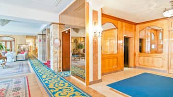 Un vestíbulo de hotel con alfombra azul, paneles de madera y un espejo grande.
