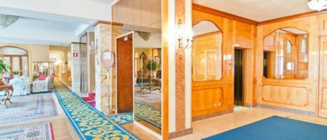 Un vestíbulo de hotel con alfombra azul, paneles de madera y un espejo grande.