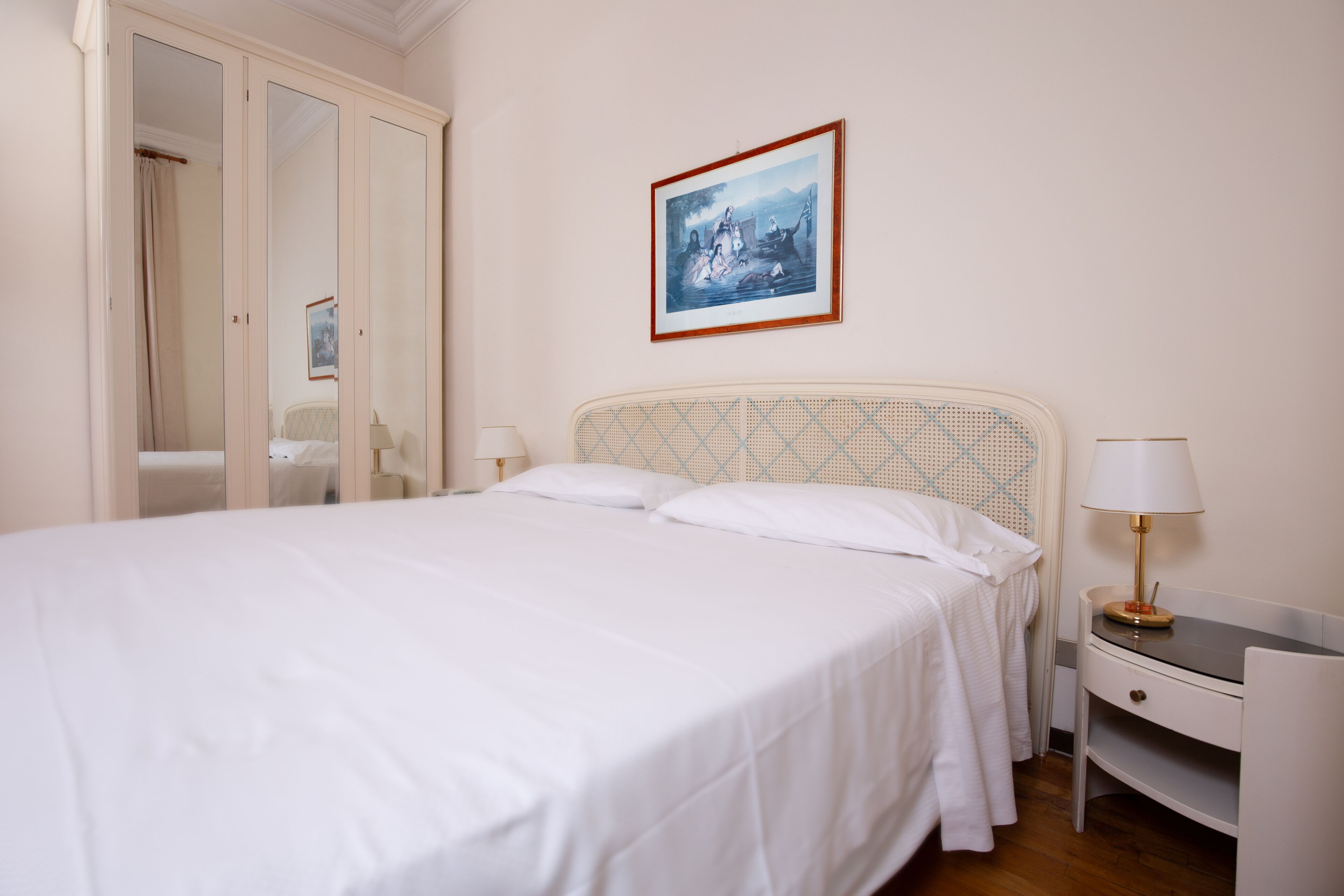 Un dormitorio con cama, mesitas de noche, un armario y un cuadro en la pared.