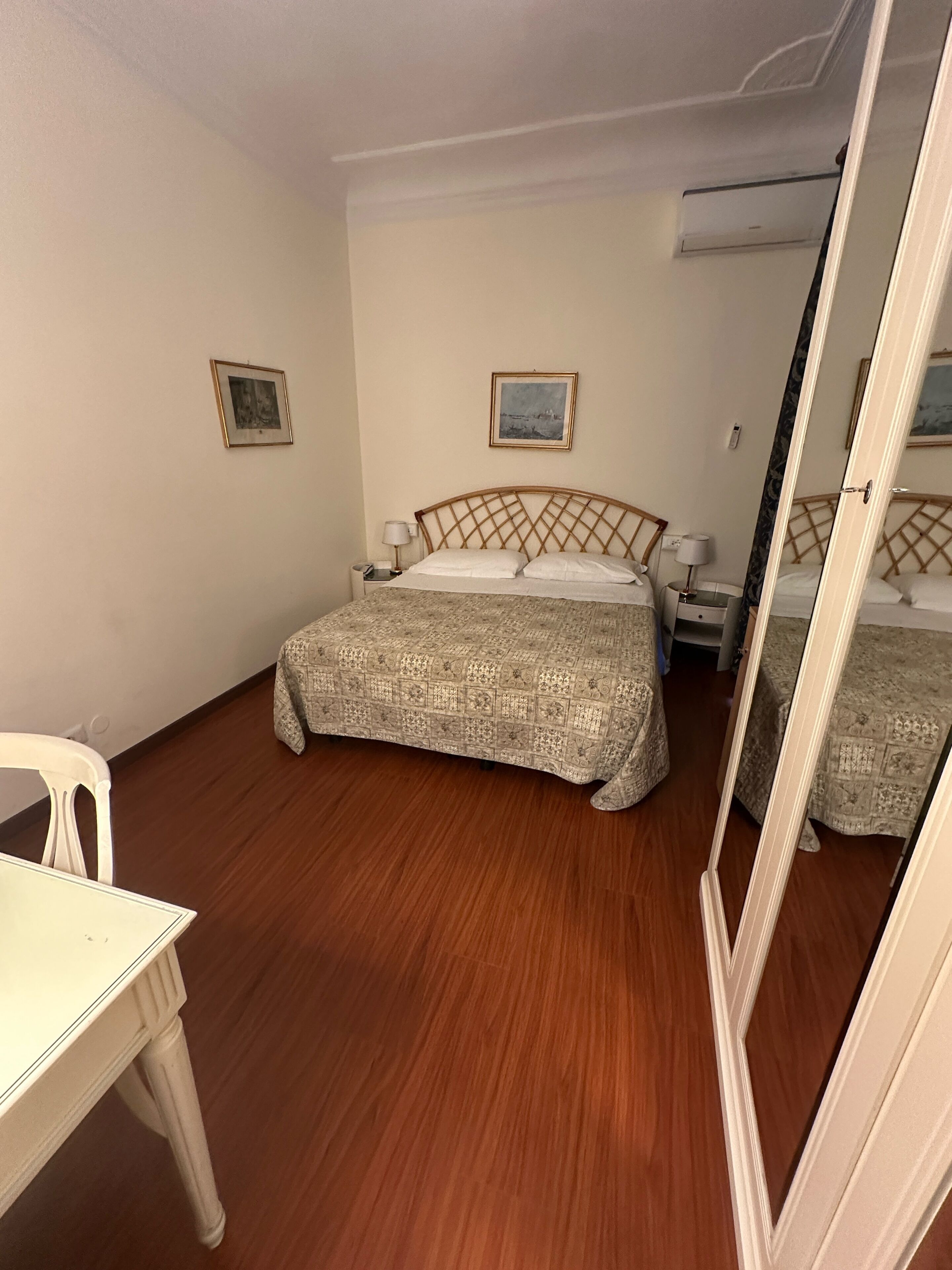 Un dormitorio con una cama de madera, una mesita de noche, una silla y dos cuadros en la pared.