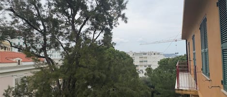 Edifício residencial com varanda, uma grande árvore em primeiro plano e vista ampla do bairro ao redor.