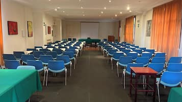 A conference room with rows of blue chairs, a projector screen, and a podium.