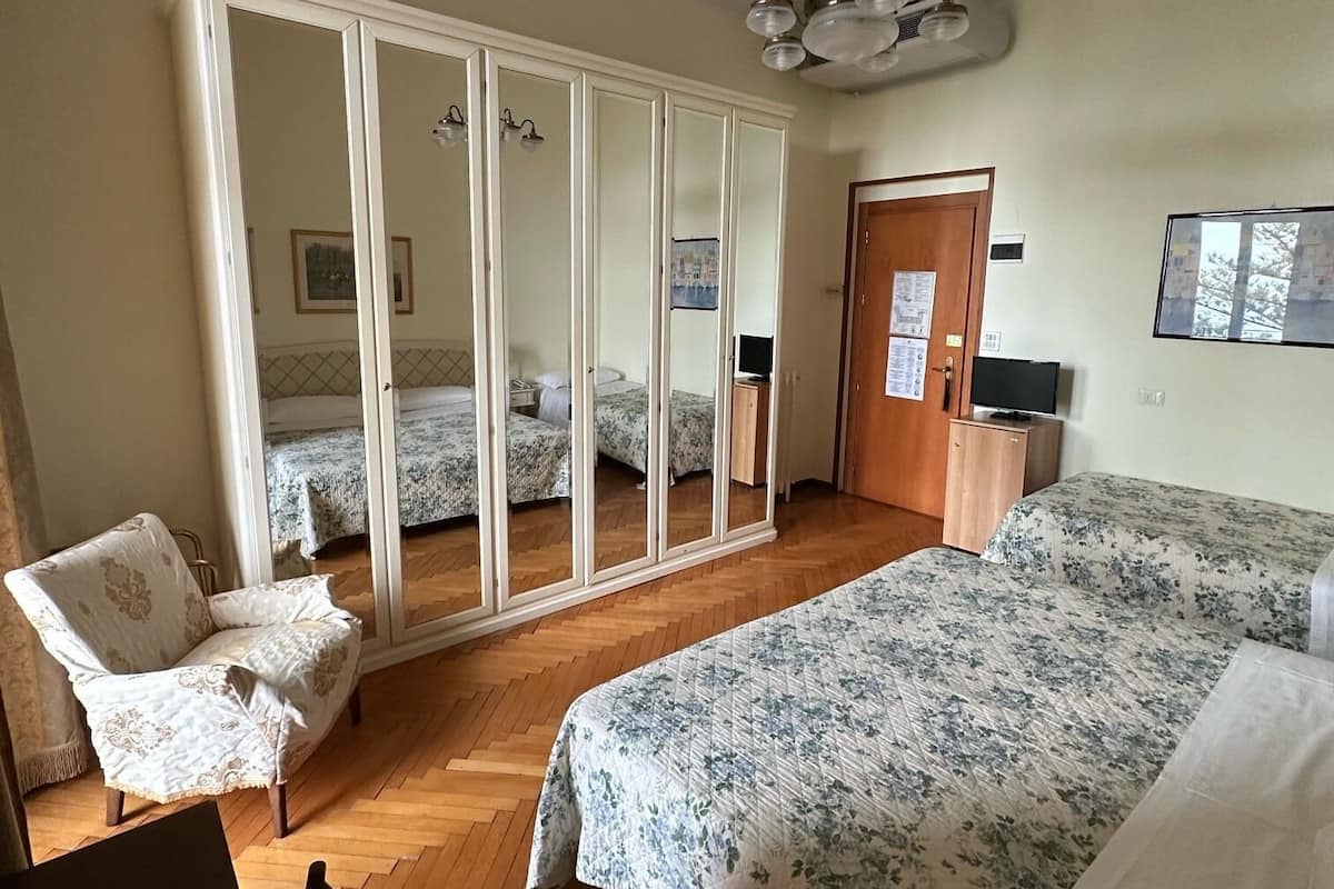 Een slaapkamer met een grote kast, een bed met bloemenbedrukking, een stoel en een bureau met een afstandsbediening.